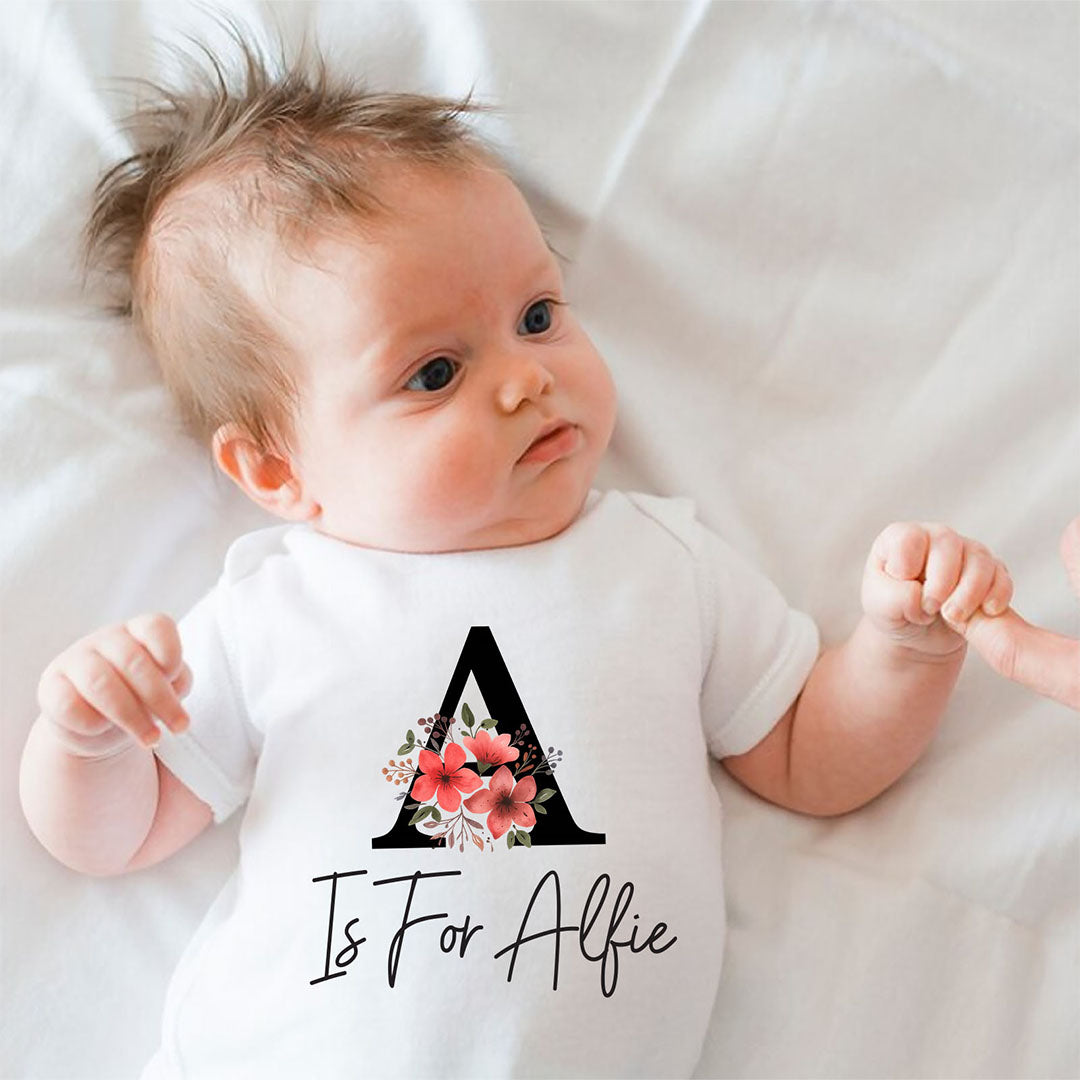 Cute baby wearing a custom white onesie with a floral "A is for Alfie" print, perfect for newborn photoshoots or baby showers.