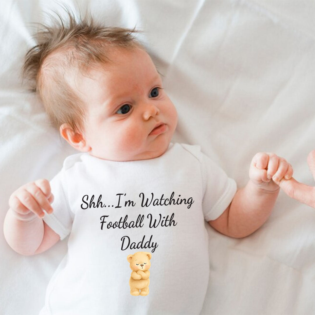 Cute baby wearing a white onesie with a teddy bear and the text ‘Shh…I’m Watching Football With Daddy’. Perfect for football game days and family bonding.