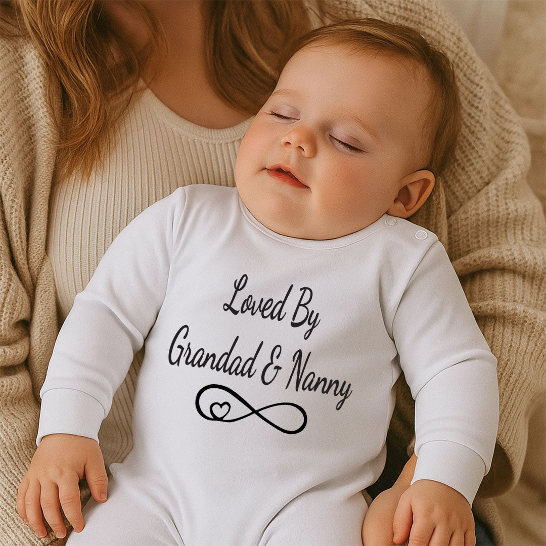Baby wearing a white onesie with 'Loved By Grandad & Nanny' text, sitting on a soft surface.