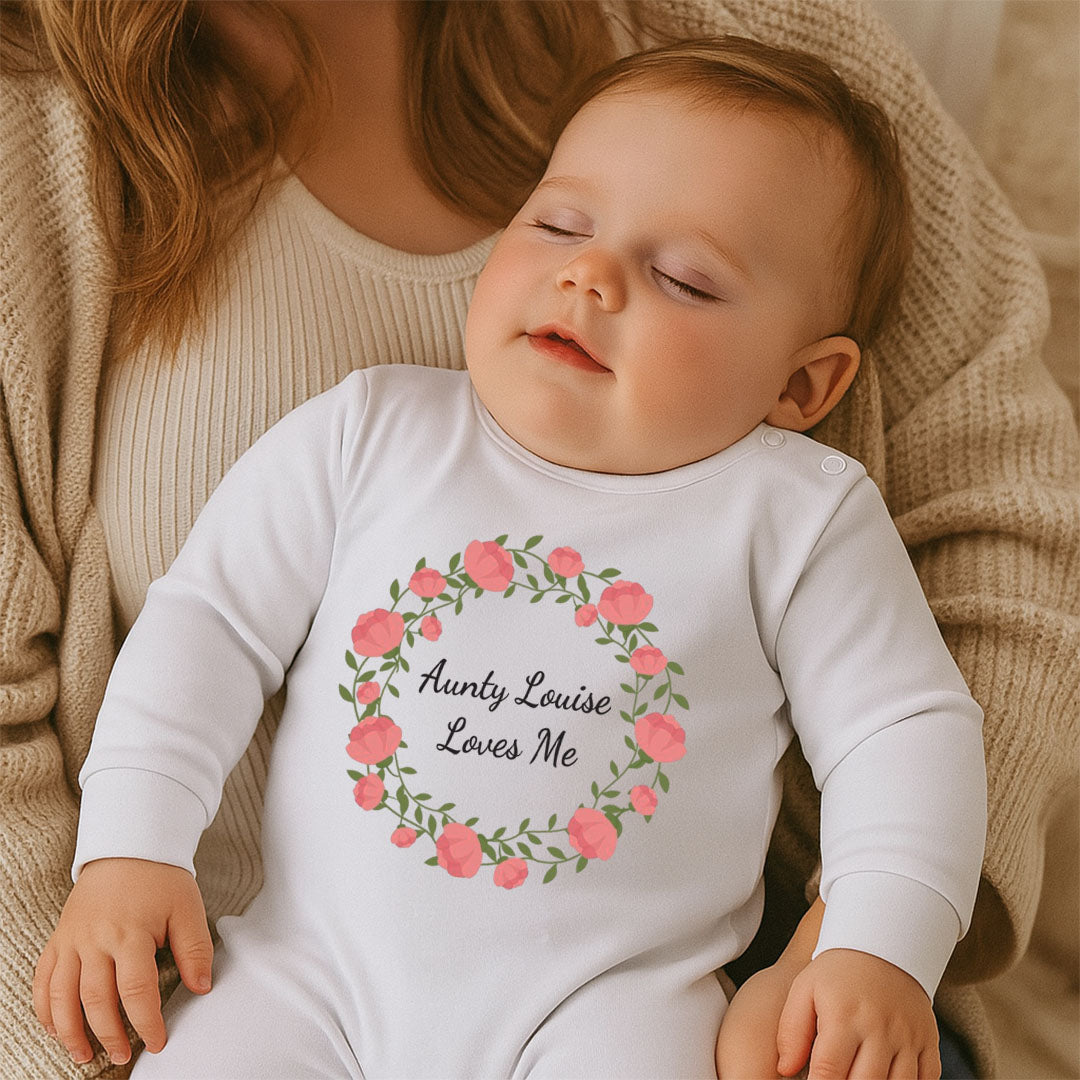 Baby wearing a white onesie with floral design and text, sitting on a soft surface.