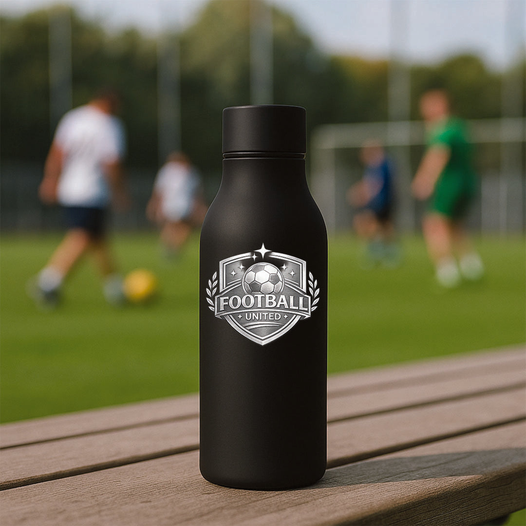 Black water bottle with 'Football United' logo on a wooden table with a blurred soccer field background