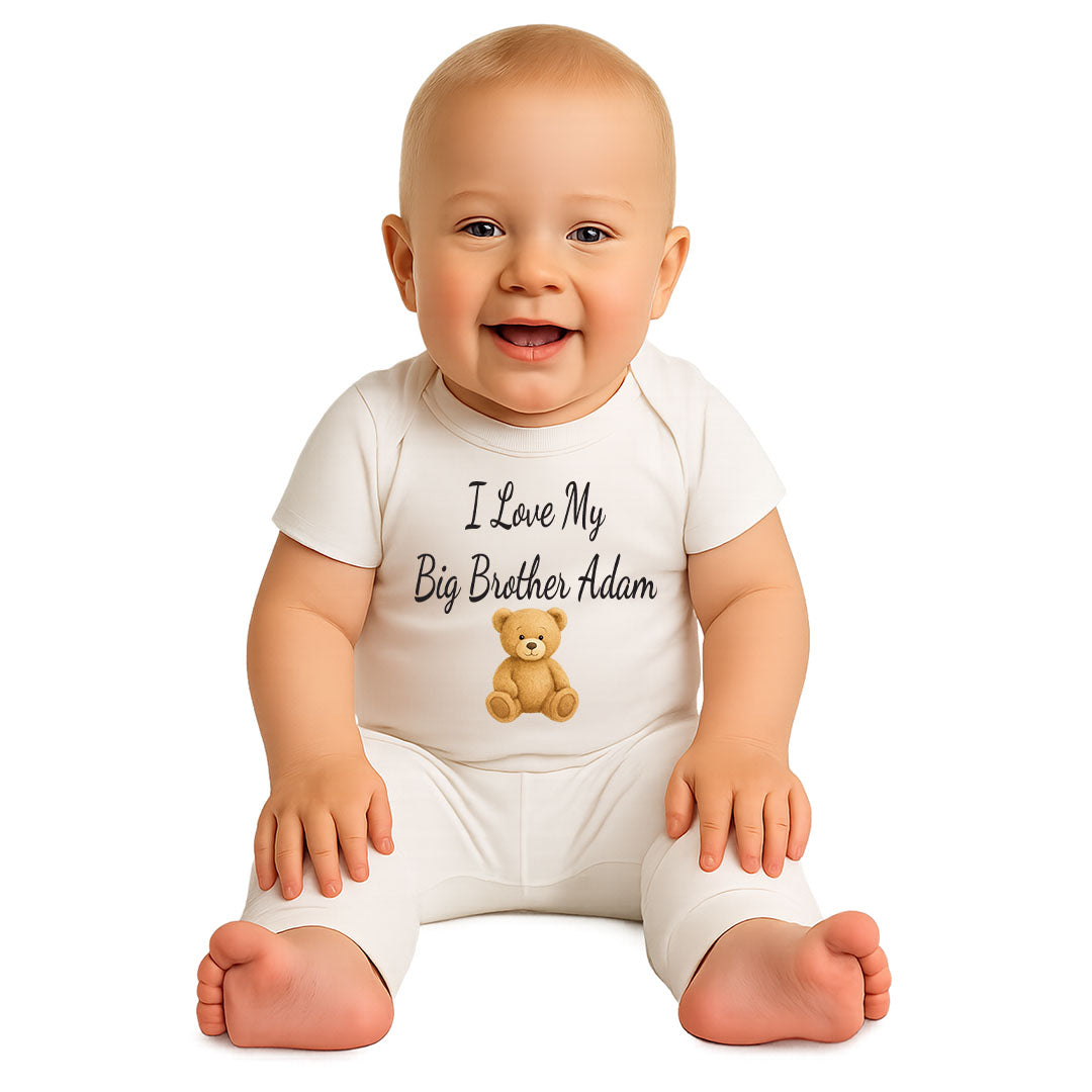 Adorable baby wearing a white onesie featuring the text "I Love My Big Brother Adam" and a cute teddy bear illustration, sitting and smiling on a white background.