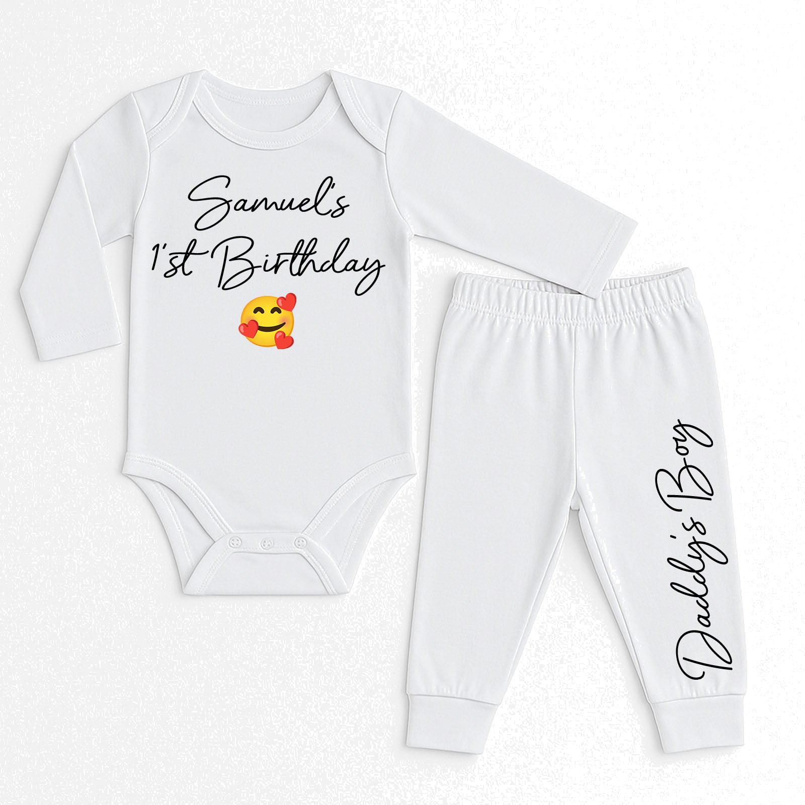 A two-piece baby outfit set consisting of a long-sleeve white bodysuit and matching jogger pants. The bodysuit features the text 'Samuel's 1st Birthday' in black script with a yellow and red smiling emoji graphic.