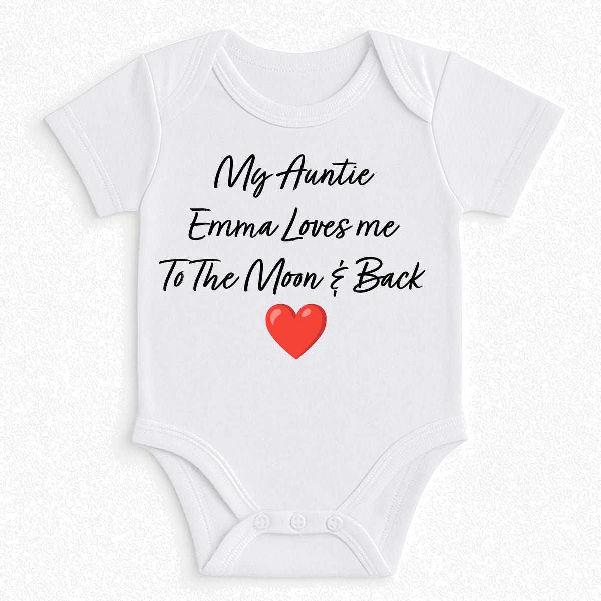 A white short-sleeve baby bodysuit with black cursive text reading 'My Auntie Emma Loves me To The Moon & Back' and a red heart graphic on the front, shown on a light textured background.