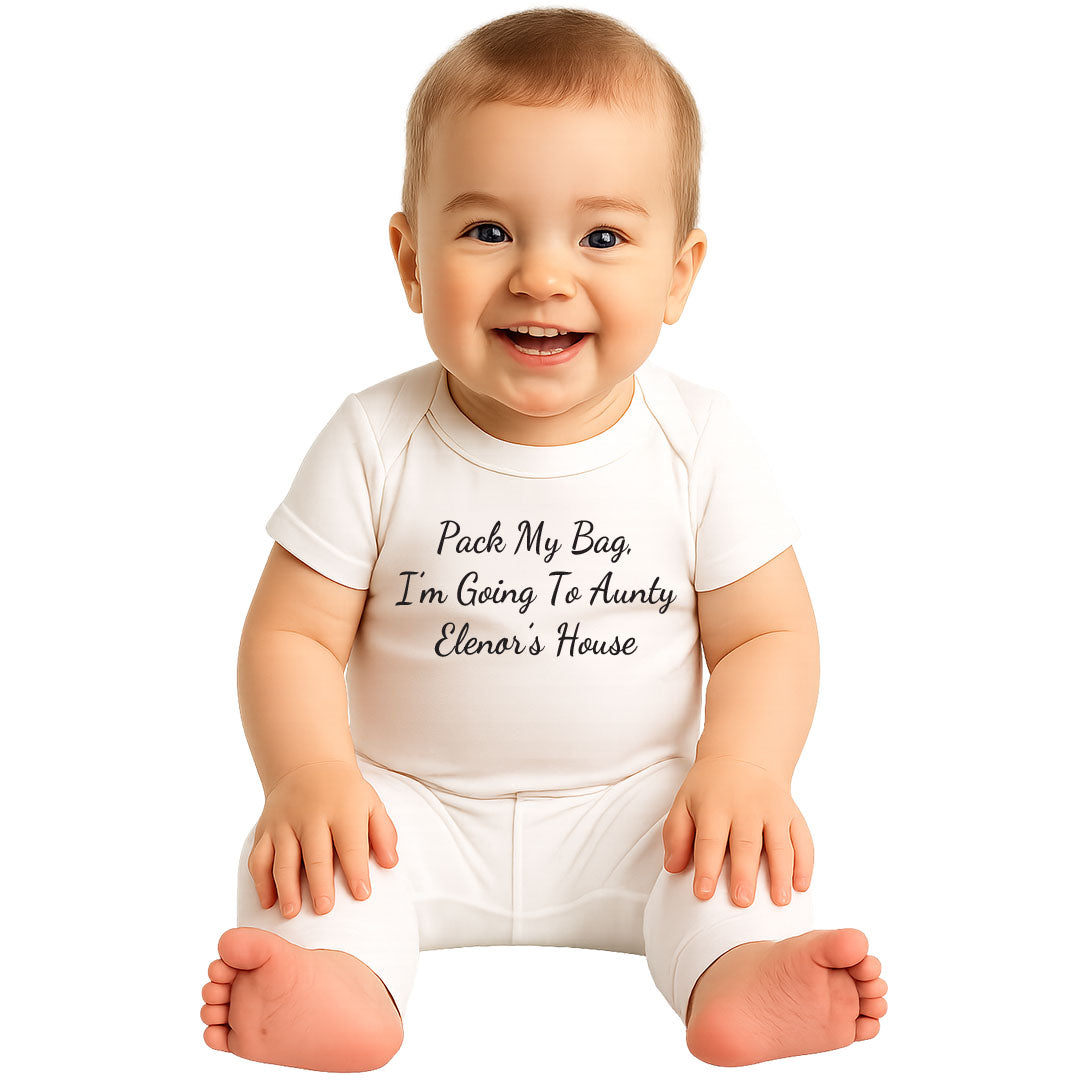 Smiling baby wearing a white onesie with the humorous text "Pack My Bag, I'm Going To Aunty Elenor's House" printed on the front, sitting happily against a white background.