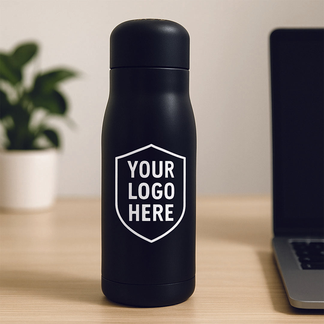 Black water bottle with 'Your Logo Here' text on a desk with a laptop and plant in the background