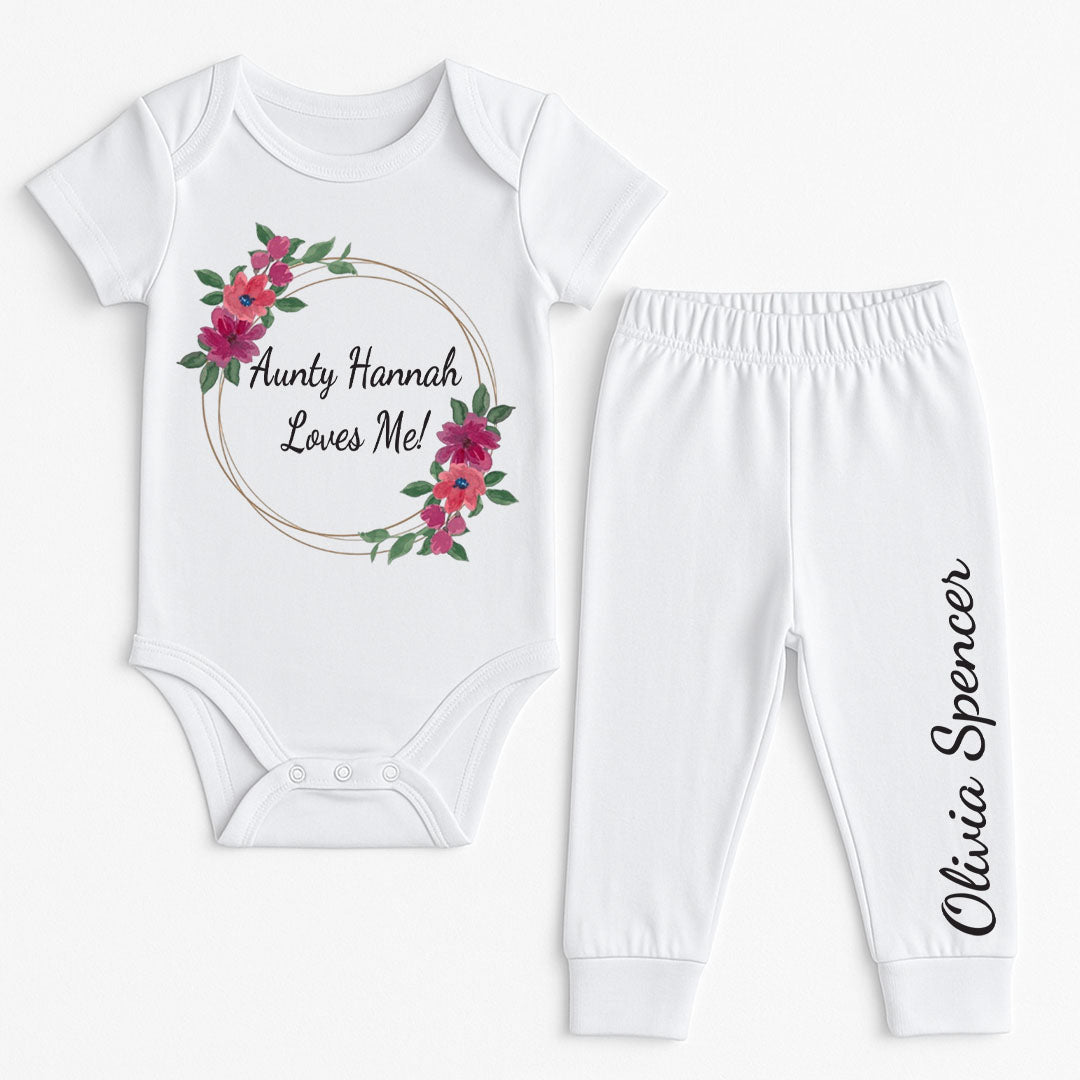 White baby vest and pants set featuring a pink floral wreath with the text "Aunty Hannah Loves Me!" and custom name "Olivia Spencer" printed on the leg.