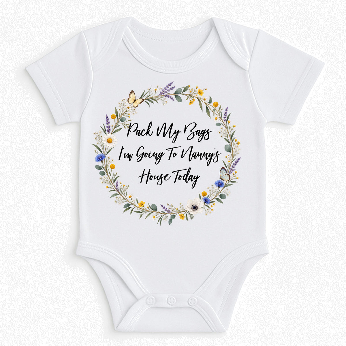 White short-sleeve baby bodysuit with a floral wreath graphic and the text 'Pack My Bags I'm Going To Manny's House Today' printed on the front, shown on a light textured background.