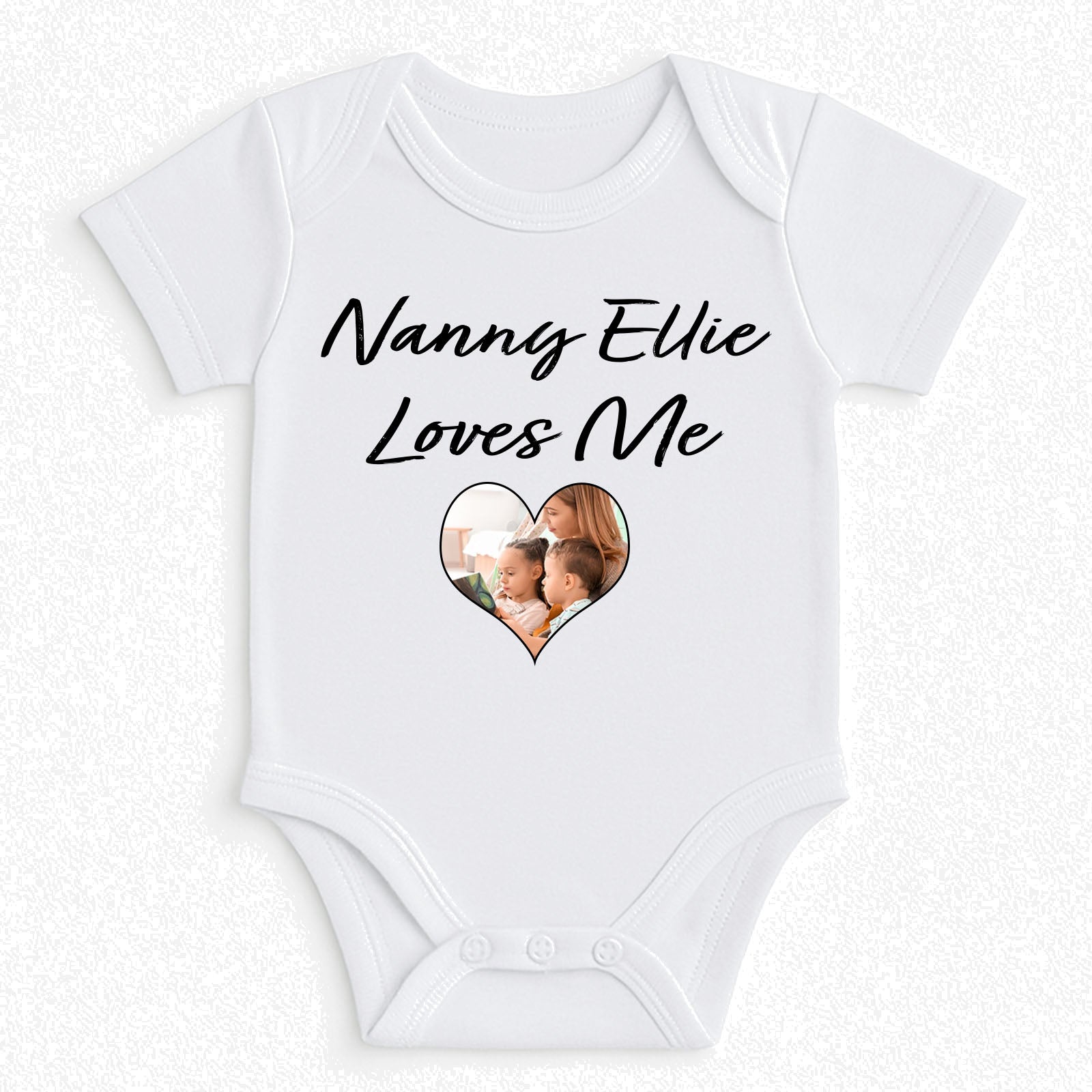 A white short-sleeve baby bodysuit with 'Nanny Ellie Loves Me' printed in black script above a heart-shaped photo window on the front, displayed flat against a light textured background.
