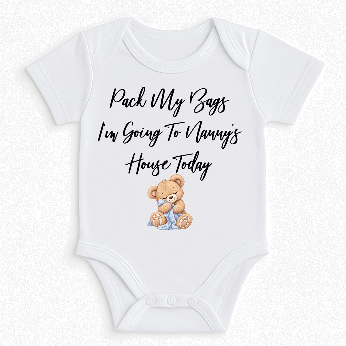 A white short-sleeve baby bodysuit with the text 'Pack My Bags I'm Going To Nanny's House Today' in black script, plus a small teddy bear illustration sitting in blue pants. The bodysuit is shown flat against a light textured background.