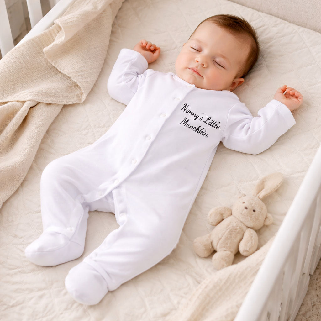 Baby in a white onesie with text, lying on a beige blanket next to a plush toy.